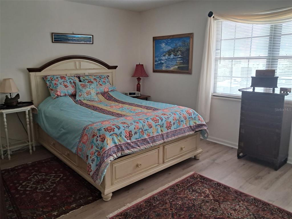A bedroom features a queen bed with floral bedding, a wooden dresser, and area rugs — 1922 S RIVERSIDE DRIVE, EDGEWATER, FL