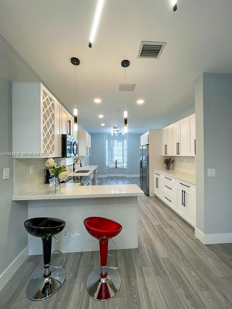 A modern kitchen features white cabinetry, a breakfast bar with two stools, and light flooring — 1261 Hayes St, Hollywood FL 33019, HOLLYWOOD, FL