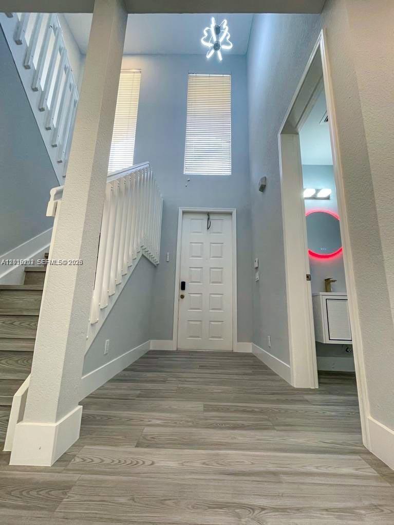 A bright entryway features a staircase, light wood-look flooring, and a doorway to a bathroom — 1261 Hayes St, Hollywood FL 33019, HOLLYWOOD, FL