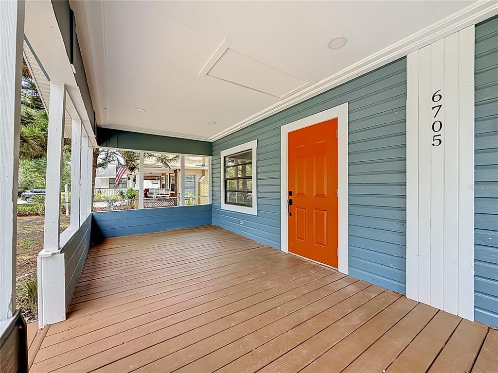 A covered front porch features blue horizontal siding, a bright orange door, and wooden decking — 6705 N ELIZABETH STREET, TAMPA, FL