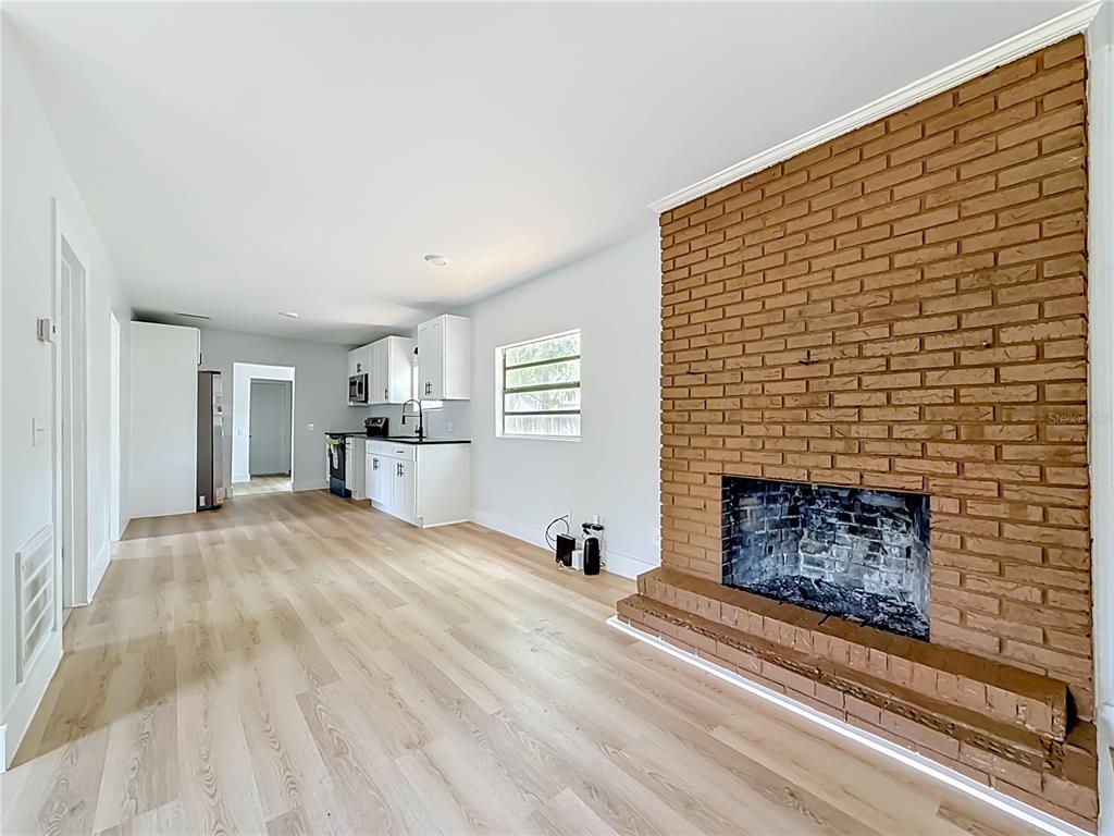 A living room with light wood flooring and a large red brick fireplace — 6705 N ELIZABETH STREET, TAMPA, FL