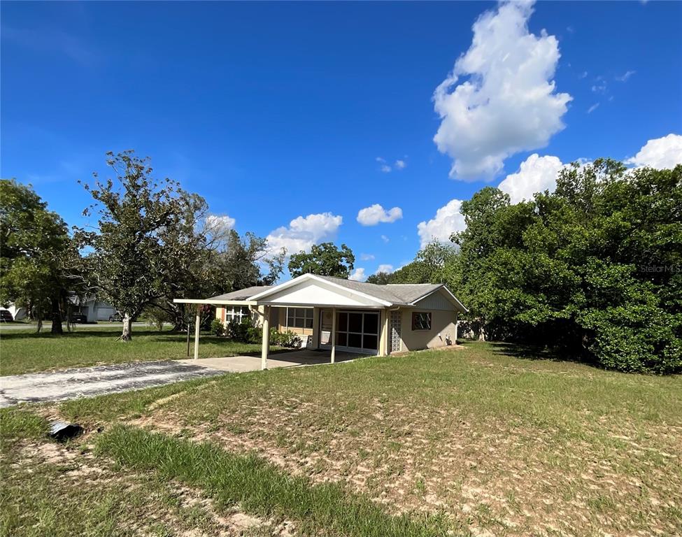 A single-story house with a carport and a large, grassy yard under a blue sky — 9359 BAHIA ROAD, OCALA, FL