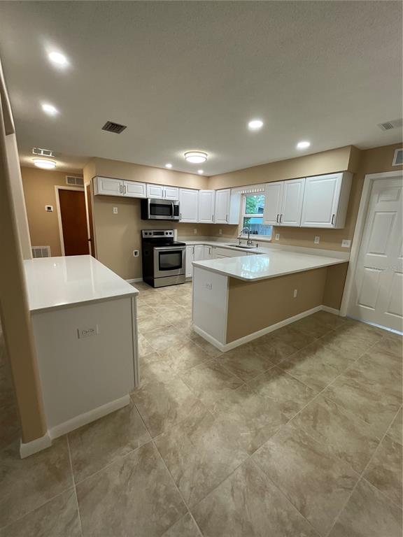 A kitchen features white cabinets, stainless steel appliances, and light-colored countertops over tile flooring — 9359 BAHIA ROAD, OCALA, FL