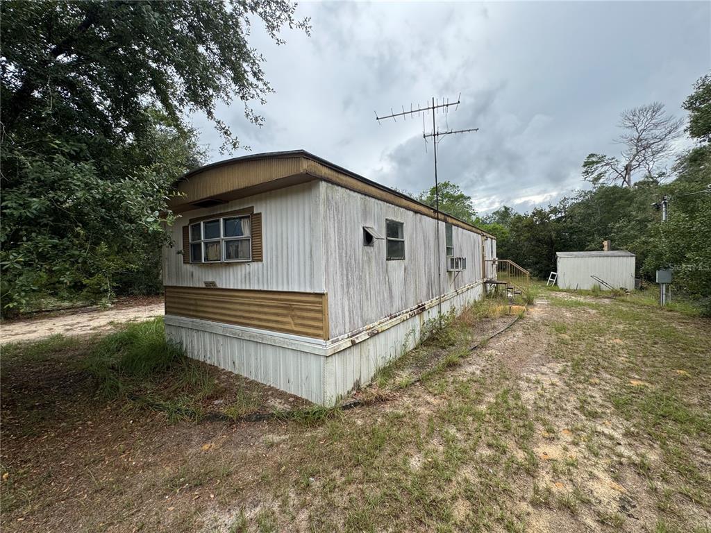 An exterior view of a weathered mobile home with a metal antenna and small shed — 23180 NE 156TH COURT, FORT MC COY, FL