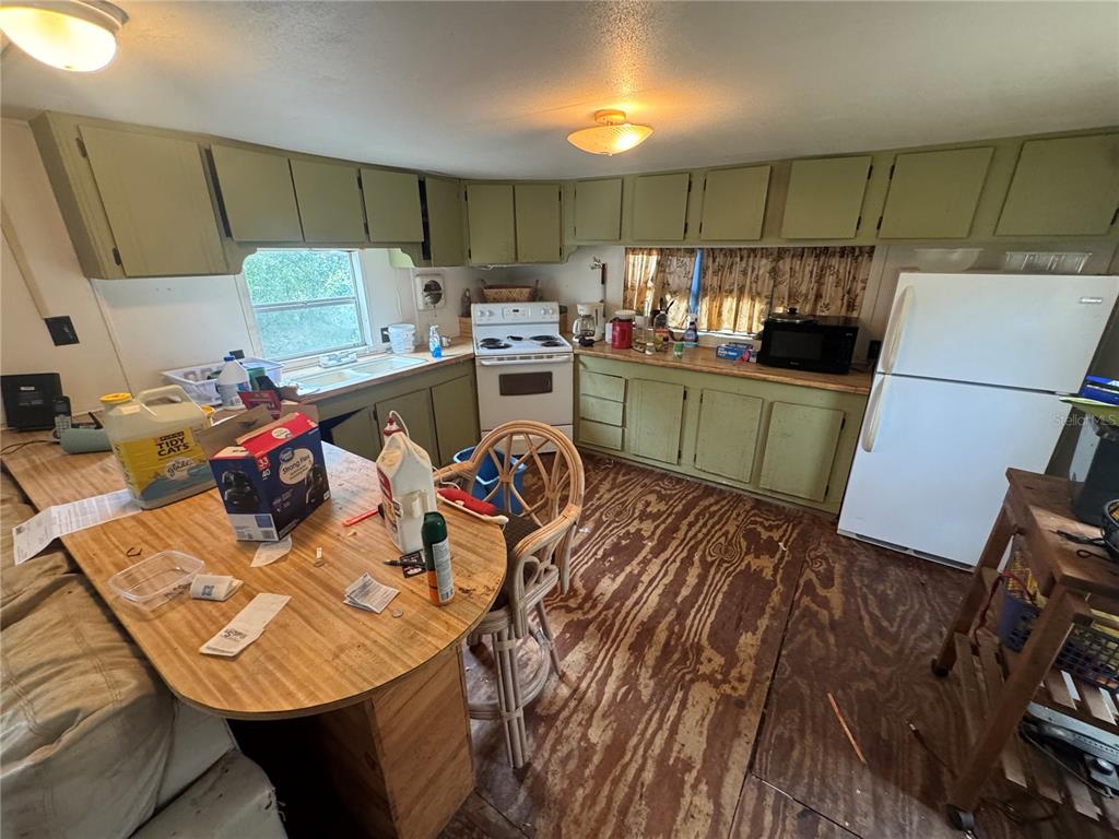 A kitchen features olive green cabinets, a white stove, a white refrigerator, and plywood flooring — 23180 NE 156TH COURT, FORT MC COY, FL