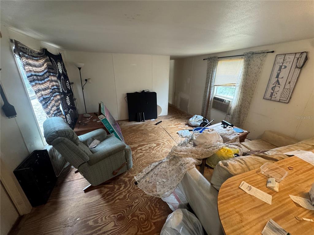 A living room with exposed plywood subflooring, a recliner, a sofa, and a window air conditioner — 23180 NE 156TH COURT, FORT MC COY, FL