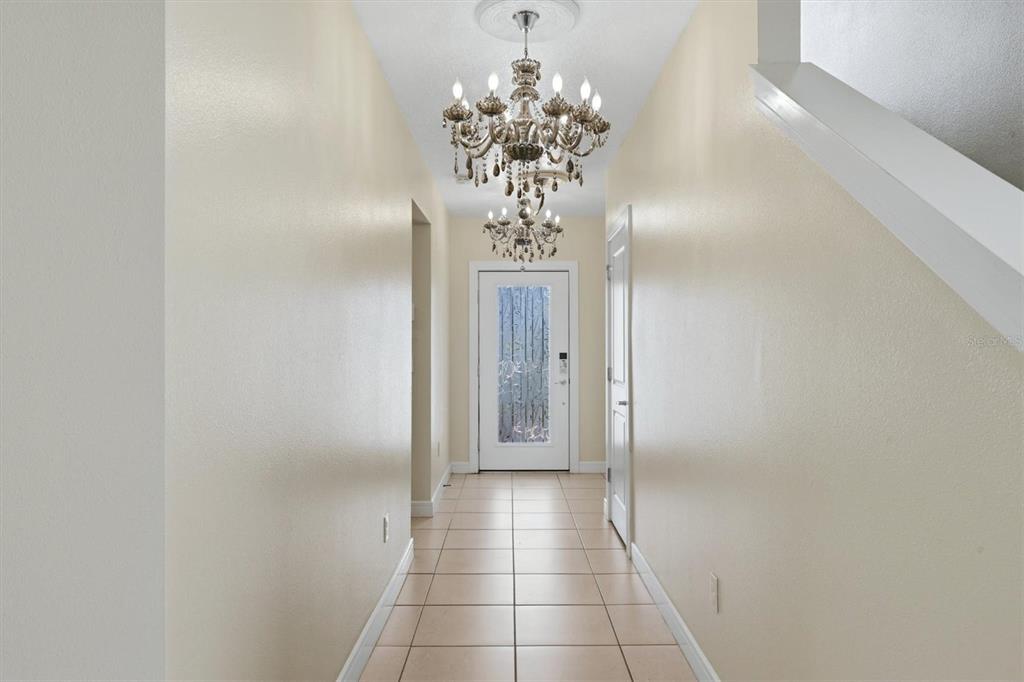 A hallway with tile flooring, beige walls, and a tiered crystal chandelier leads to a door — 9108 ROYAL RIVER CIRCLE, PARRISH, FL