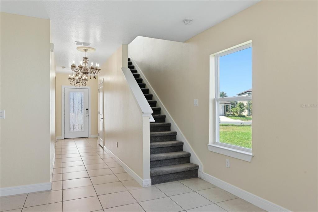 An entryway features a tiled floor, a staircase with gray carpet, and a crystal chandelier — 9108 ROYAL RIVER CIRCLE, PARRISH, FL