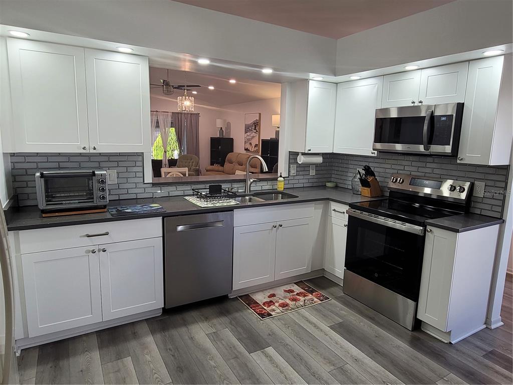 A kitchen with white cabinets, gray subway tile backsplash, stainless steel appliances, and dark countertops — 14277 PALM TERRACE, PORT CHARLOTTE, FL