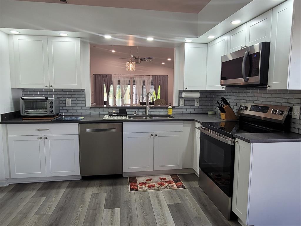 A kitchen with white cabinets, gray subway tile backsplash, stainless steel appliances, and wood-look flooring — 14277 PALM TERRACE, PORT CHARLOTTE, FL