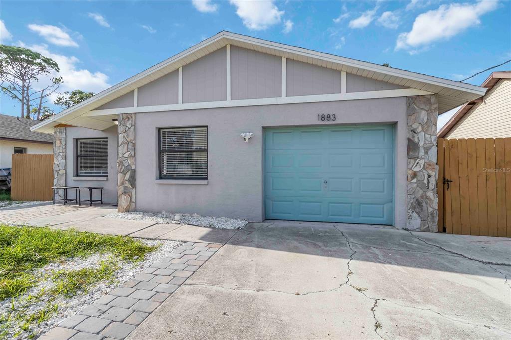 A single-story house with a light gray exterior, stone accents, and a blue garage door — 1883 MOVA STREET, SARASOTA, FL