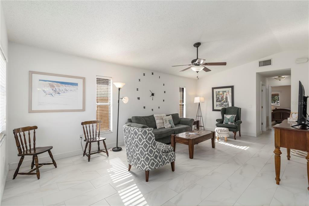 A living room features white tile floors, a grey sofa, patterned armchair, and wall clock — 1883 MOVA STREET, SARASOTA, FL