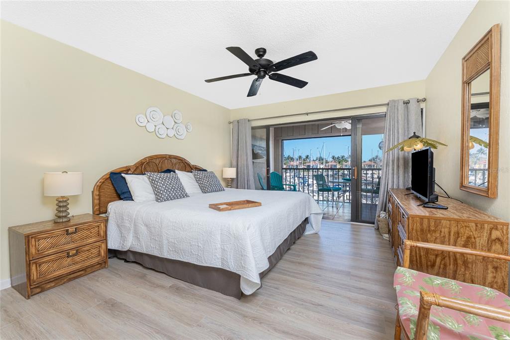 A bedroom features a rattan headboard, a ceiling fan, and a balcony overlooking a marina — 3160 MATECUMBE KEY ROAD UNIT 238, PUNTA GORDA, FL