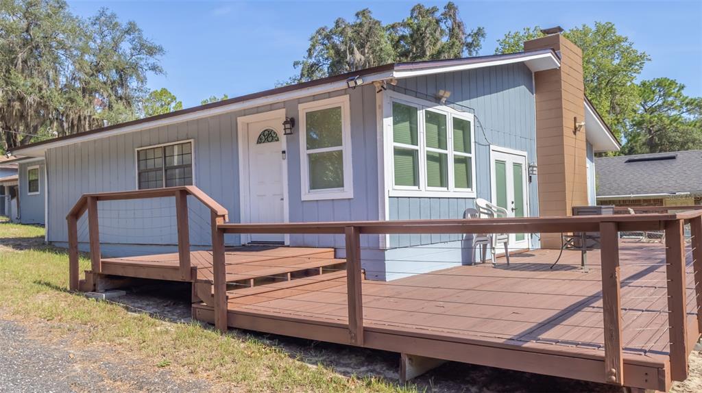 A light blue house features a large wooden deck with railings and a brick chimney — 8443 LILLY LAKE ROAD, MELROSE, FL