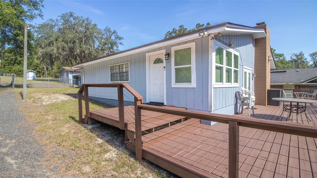 A light blue house with a wooden deck and a brown chimney under a clear sky — 8443 LILLY LAKE ROAD, MELROSE, FL