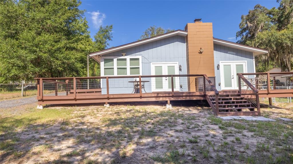 A blue house with a large wooden deck, a brick chimney, and French doors — 8443 LILLY LAKE ROAD, MELROSE, FL