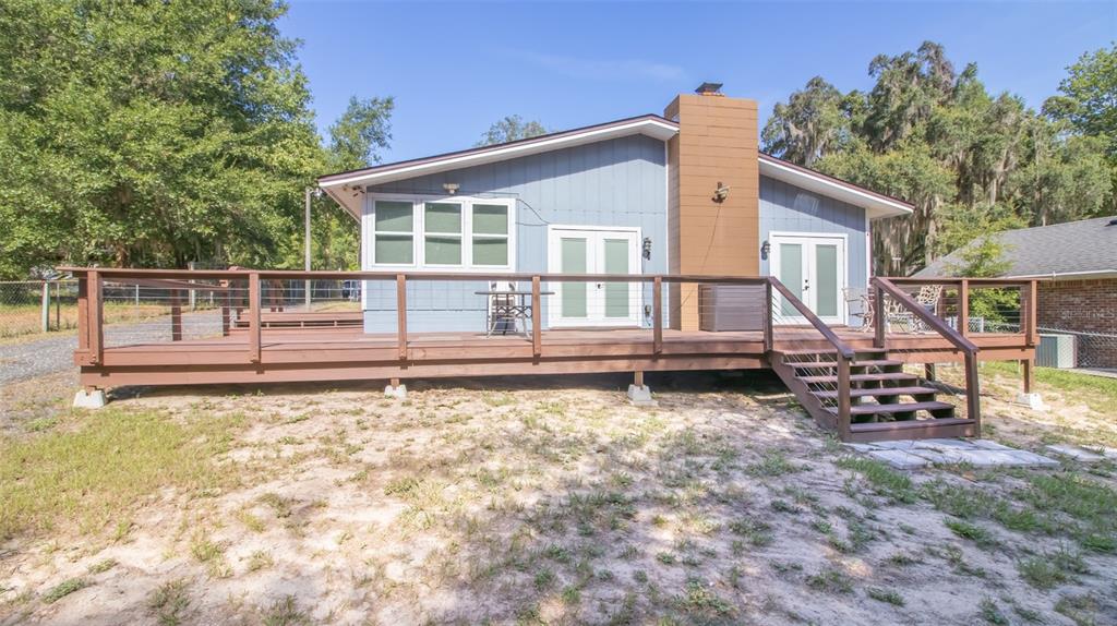 A blue house with a large wooden deck and a brick chimney exterior — 8443 LILLY LAKE ROAD, MELROSE, FL