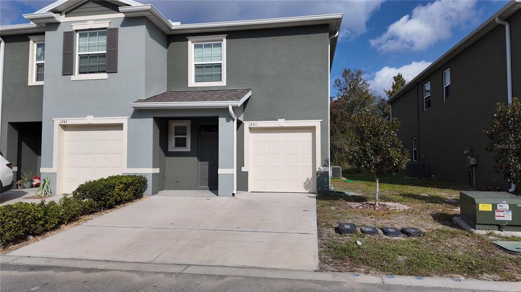 A two-story duplex features gray stucco siding, two garage doors, and a concrete driveway — 1241 YELLOW FINCH DRIVE, DAVENPORT, FL