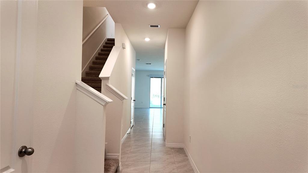 A view down a tiled hallway toward a sliding glass door with stairs on the left — 1241 YELLOW FINCH DRIVE, DAVENPORT, FL