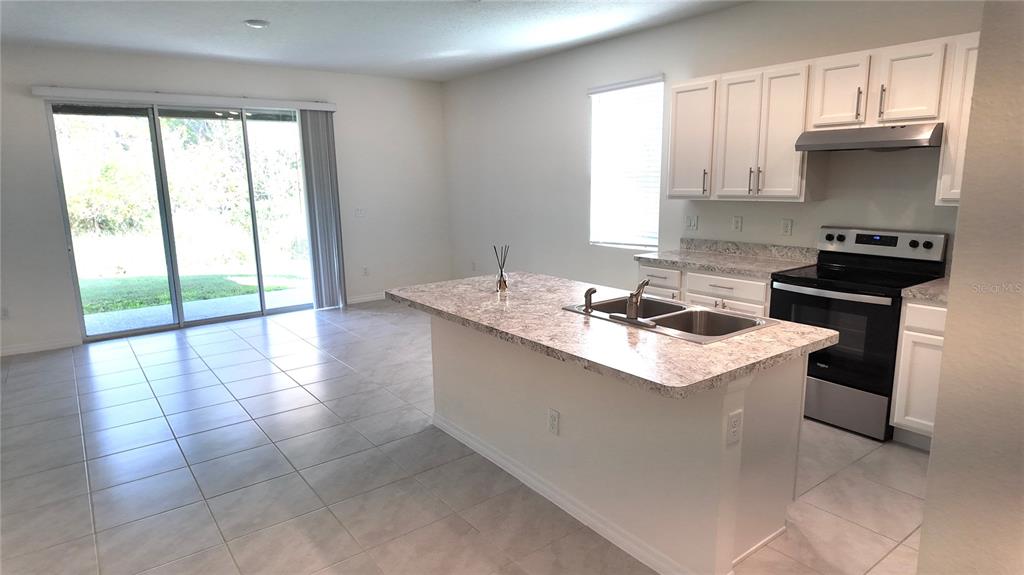 A kitchen with white cabinets, a granite-topped island, and a sliding glass door to outside — 1241 YELLOW FINCH DRIVE, DAVENPORT, FL