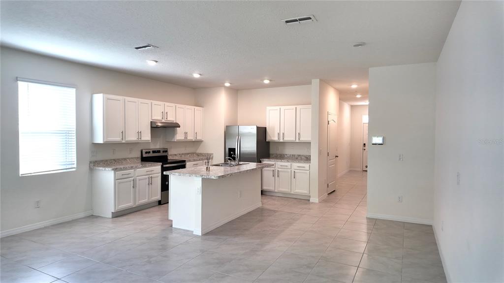 A kitchen with white cabinets, a center island, stainless steel appliances, and light-colored tile flooring — 1241 YELLOW FINCH DRIVE, DAVENPORT, FL