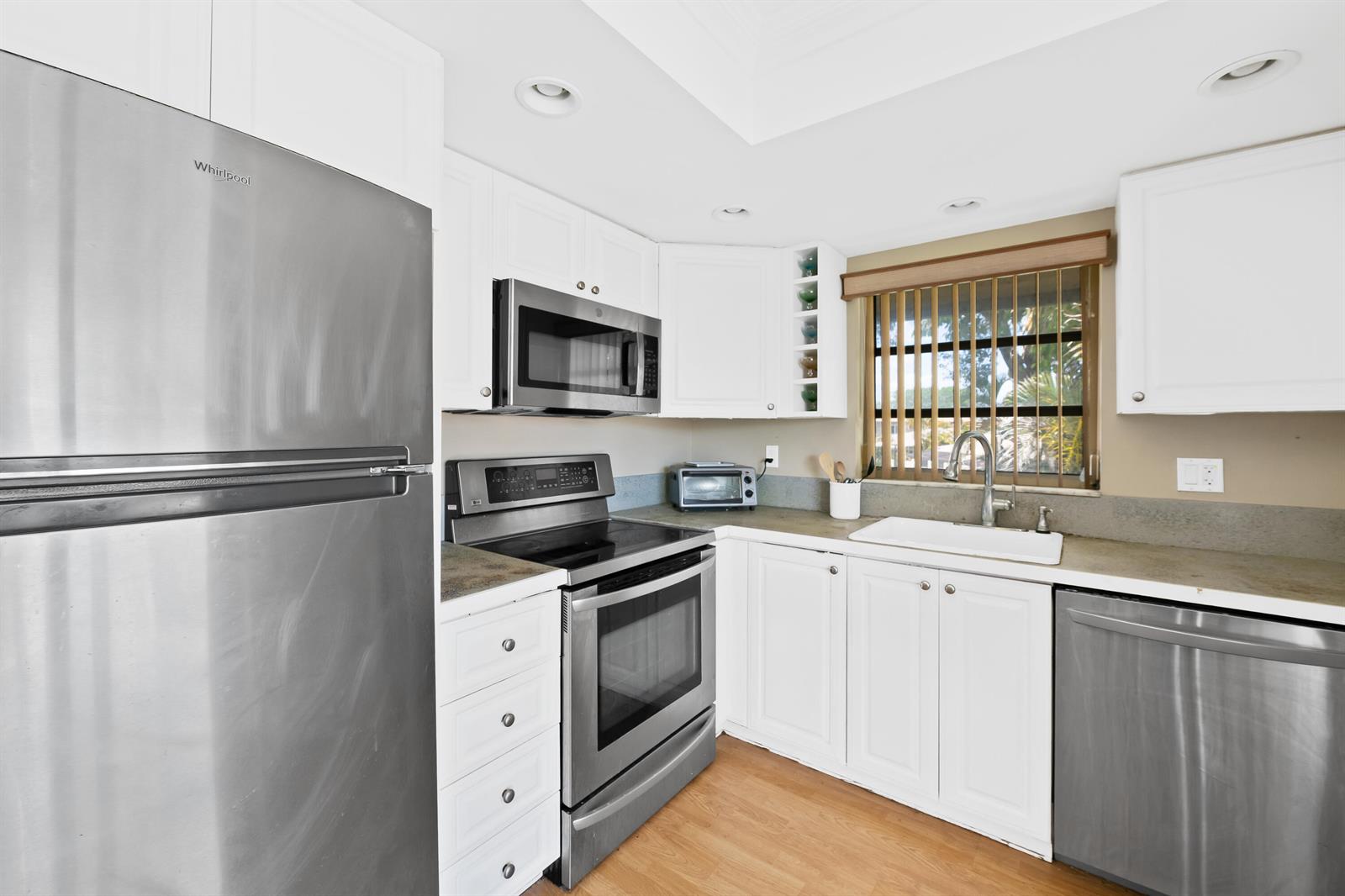 A kitchen features white cabinets, stainless steel appliances, a sink, and light wood flooring — 13771 Via Aurora, Delray Beach FL 33484, DELRAY BEACH, FL