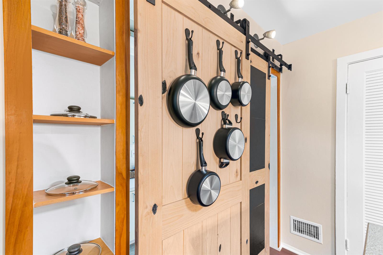 A sliding wooden barn door with hanging cookware sits beside built-in shelves in a kitchen — 303 Lang Road, Cloud Lake FL 33406, CLOUD LAKE, FL