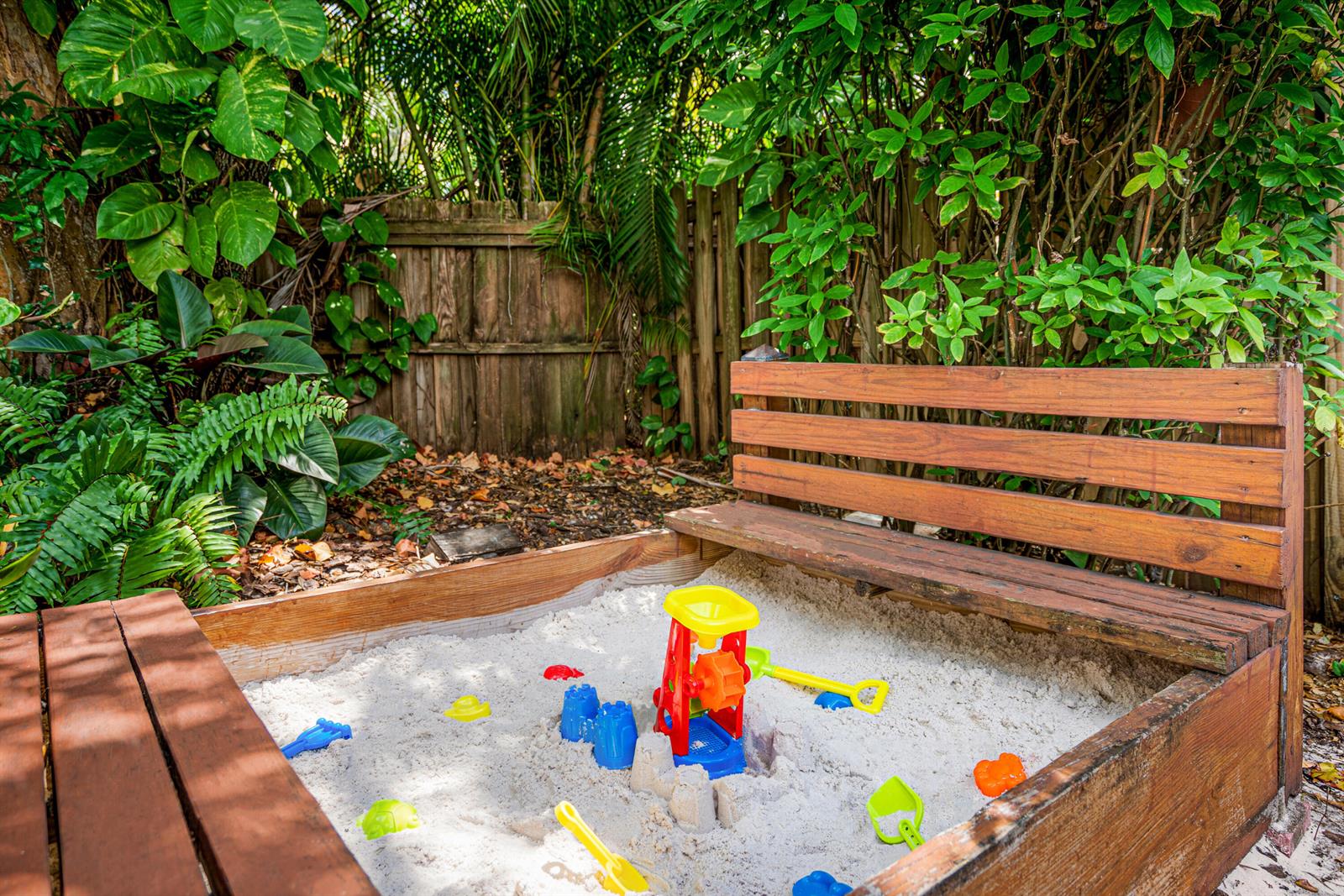 A wooden sandbox with a built-in bench sits in a backyard surrounded by lush greenery — 303 Lang Road, Cloud Lake FL 33406, CLOUD LAKE, FL