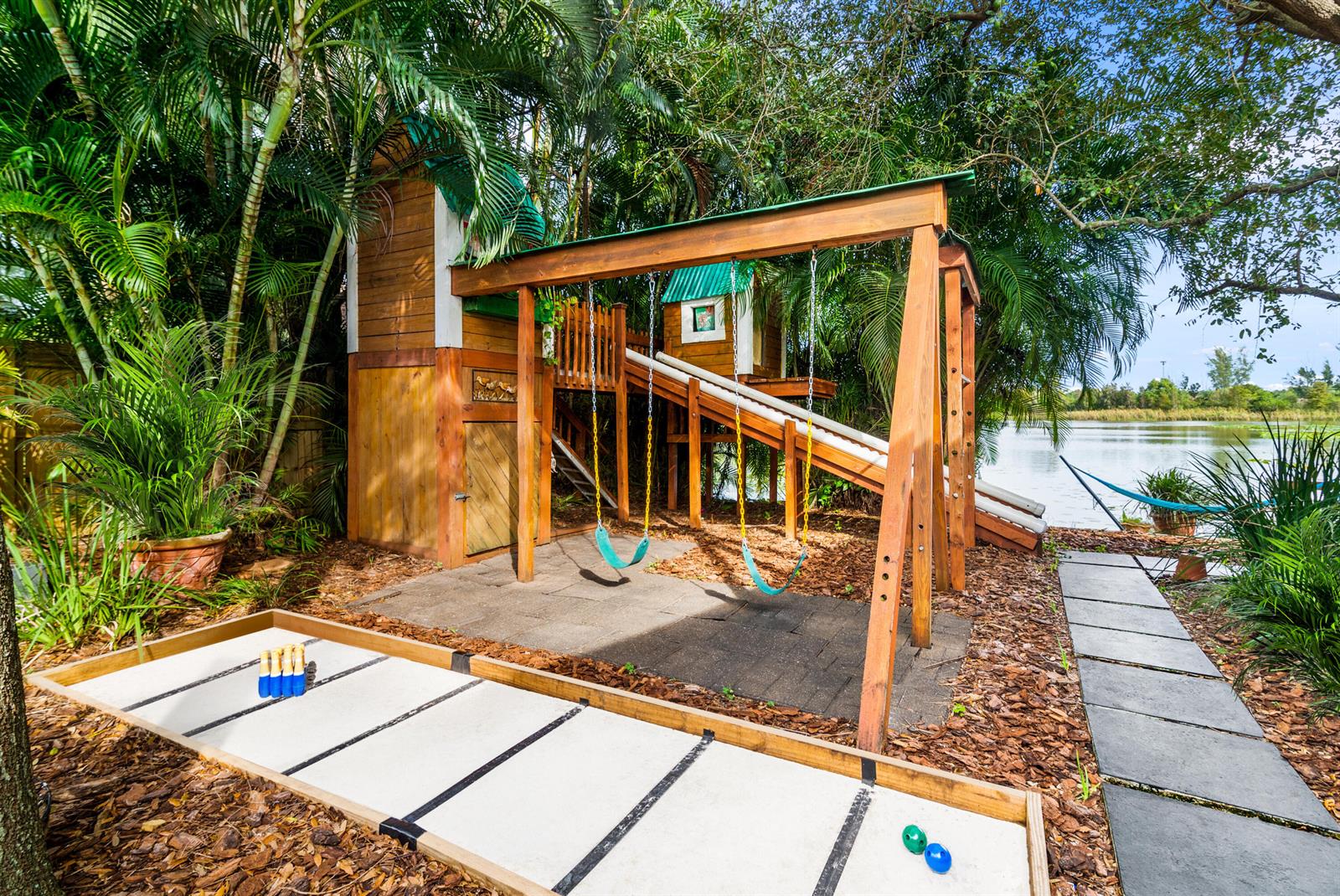 A wooden playset with swings and a slide sits next to a backyard shuffleboard court — 303 Lang Road, Cloud Lake FL 33406, CLOUD LAKE, FL