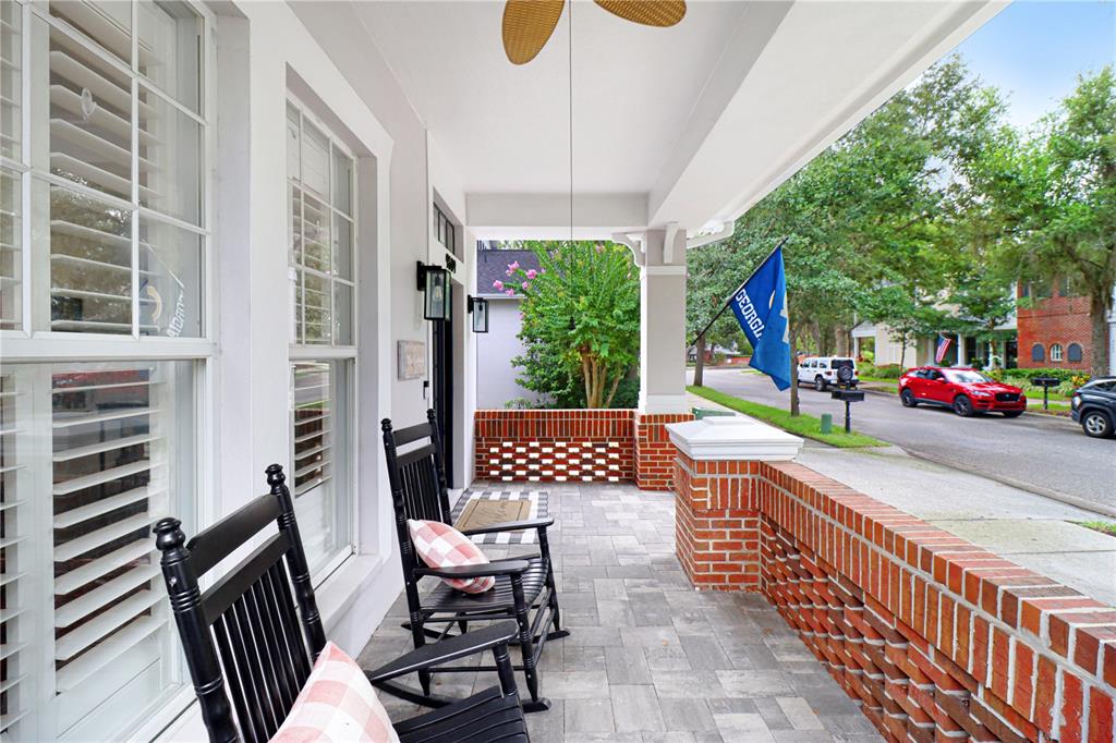 A covered front porch features brick walls, gray pavers, and two black rocking chairs — 9609 ROYCE DRIVE, TAMPA, FL