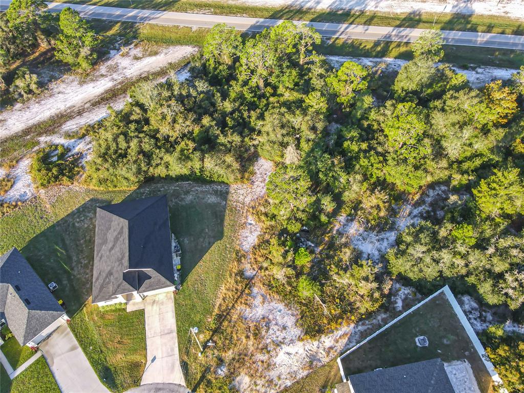 An aerial view shows a house with a driveway next to a wooded vacant lot — 1257 AMAZON LANE, POINCIANA, FL