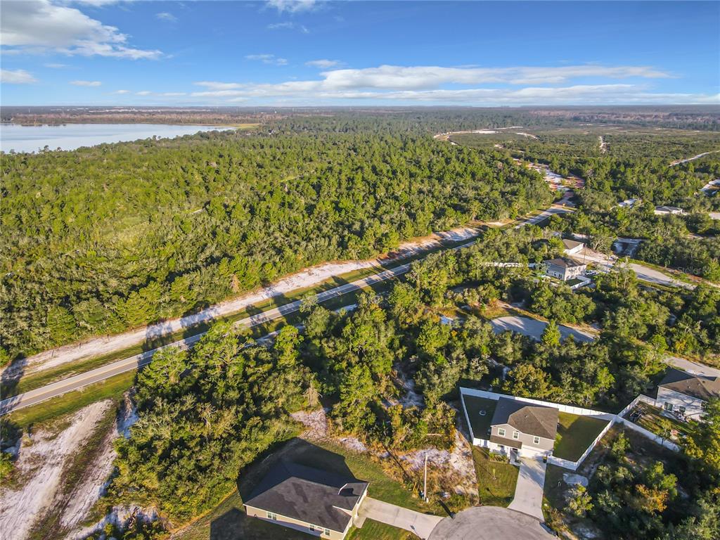 An aerial view shows two houses near a road, surrounded by dense forest and water — 1257 AMAZON LANE, POINCIANA, FL