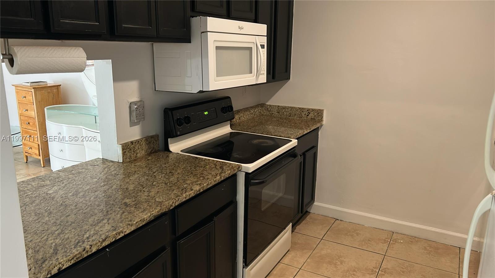 A kitchen features dark cabinets, granite countertops, a white microwave, and a black electric stove — 1855 NE 121st St # 35, North Miami FL 33181, NORTH MIAMI, FL