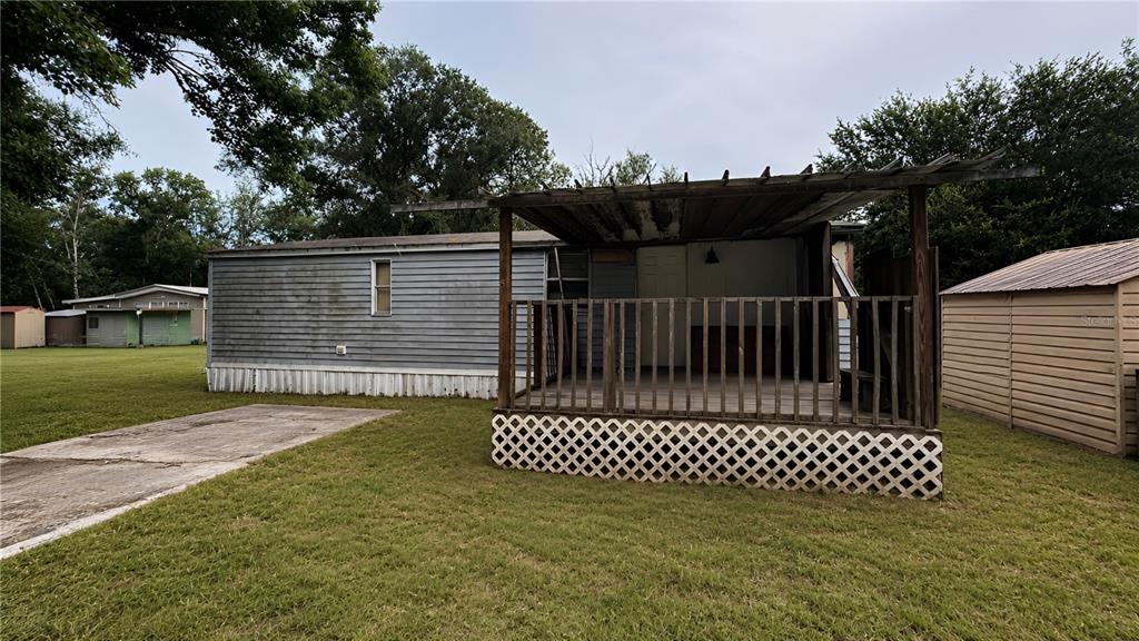 A mobile home with a wooden deck and lattice skirting sits on a grassy lot — 6408 WOODSMAN DRIVE, WESLEY CHAPEL, FL