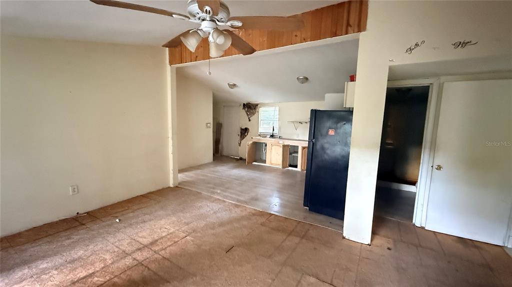 A living room leads into a kitchen with damaged walls and unfinished cabinetry — 6408 WOODSMAN DRIVE, WESLEY CHAPEL, FL