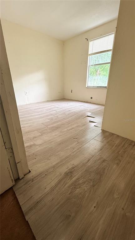 An empty room features light-colored wood-look flooring with some loose planks and a single window — 6408 WOODSMAN DRIVE, WESLEY CHAPEL, FL