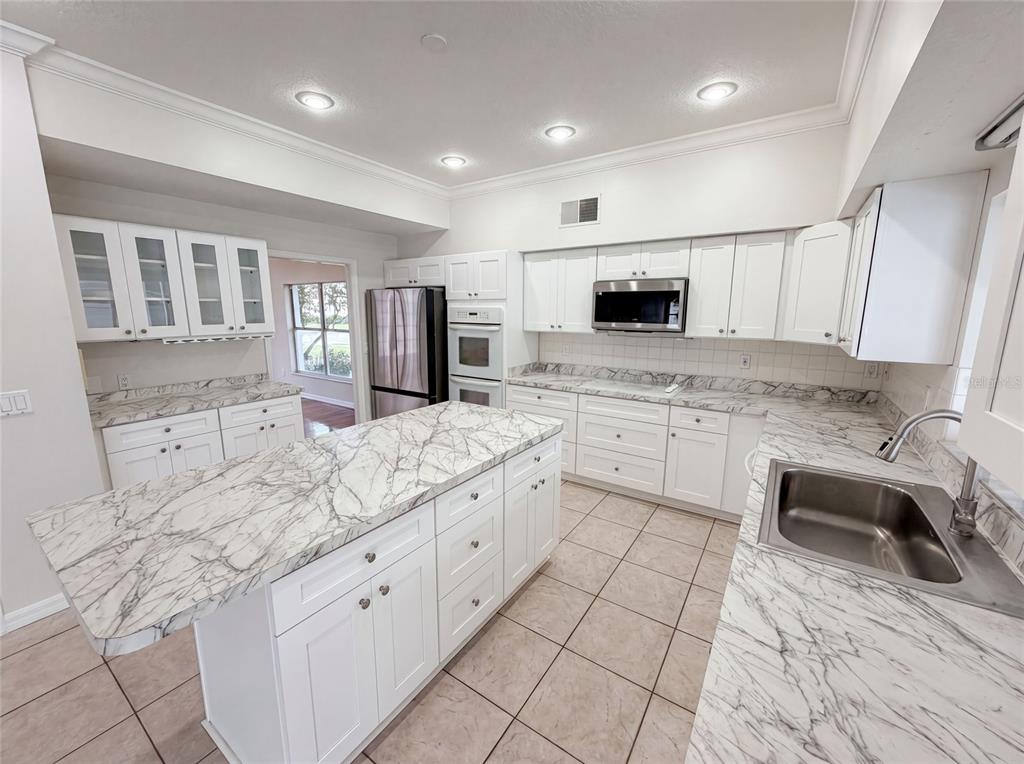 A kitchen features white cabinets, marble-patterned countertops, a center island, and stainless steel appliances — 2270 BLOSSOMWOOD DRIVE, OVIEDO, FL