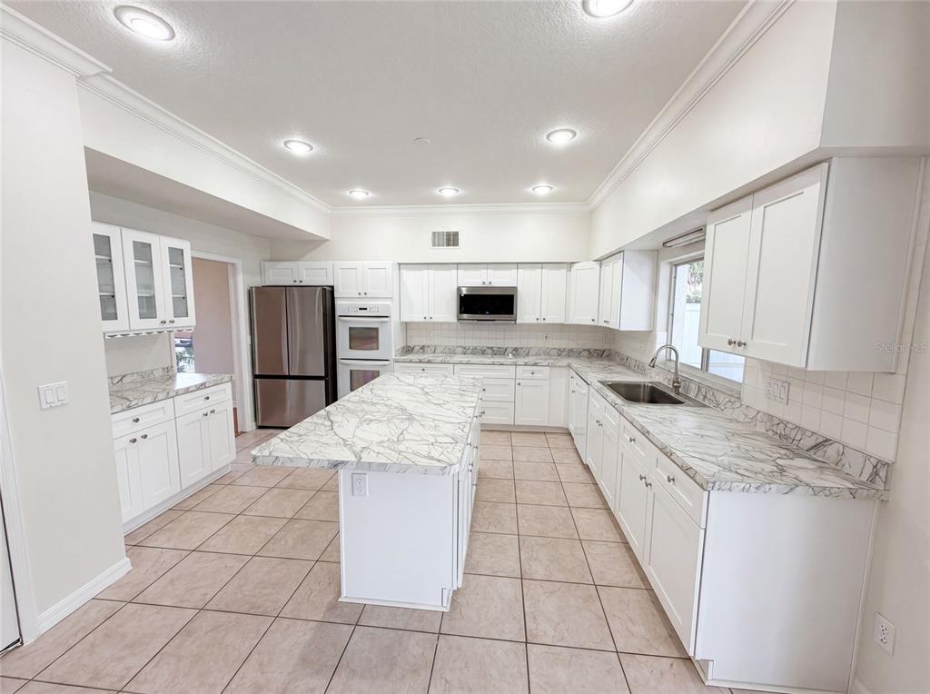 A kitchen features white cabinets, marble-patterned countertops, a central island, and tile flooring — 2270 BLOSSOMWOOD DRIVE, OVIEDO, FL