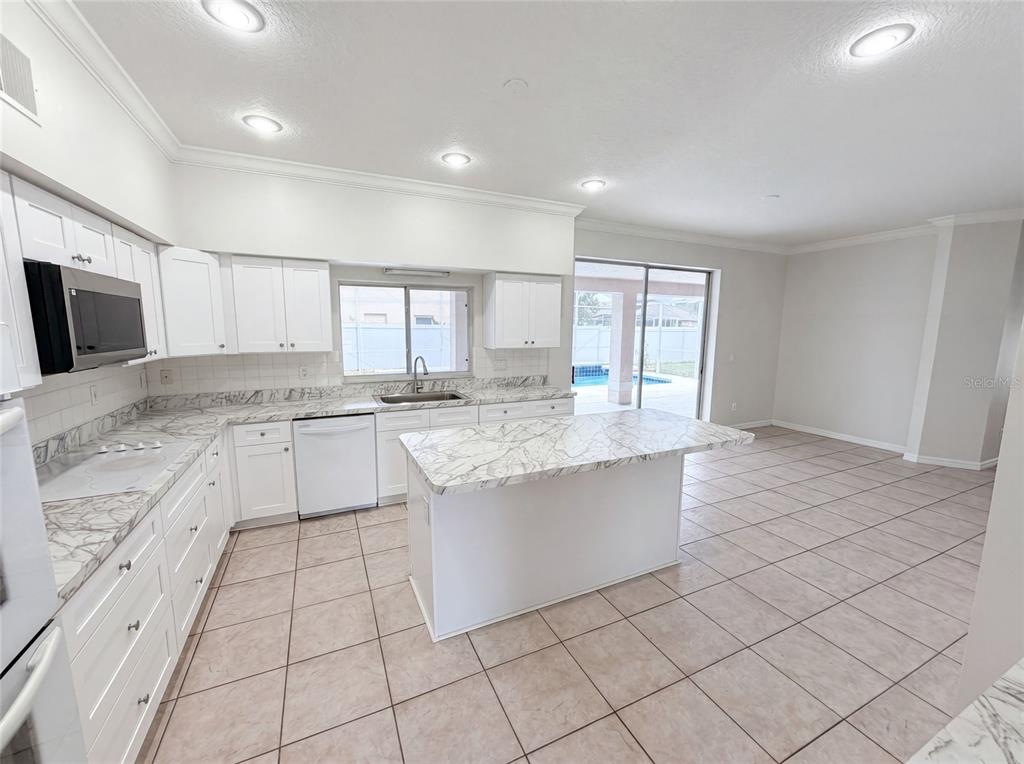 A kitchen features white cabinets, marble-patterned countertops, a center island, and tile flooring — 2270 BLOSSOMWOOD DRIVE, OVIEDO, FL