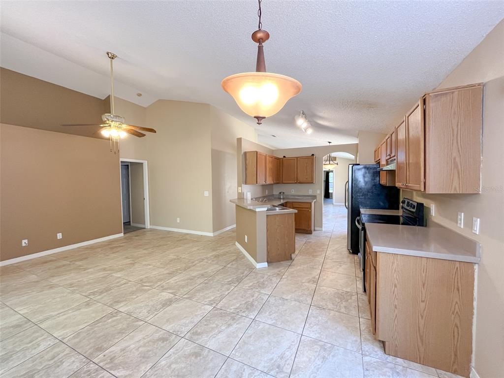 An open-concept kitchen and living area features light tile flooring and oak wood cabinets — 4397 KING EDWARD DRIVE, ORLANDO, FL