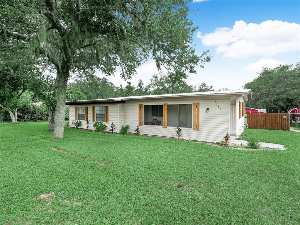 A single-story house with light siding, wood shutters, and a metal roof sits on grass — 2935 N SILVER SPUR LOOP, LAKE WALES, FL