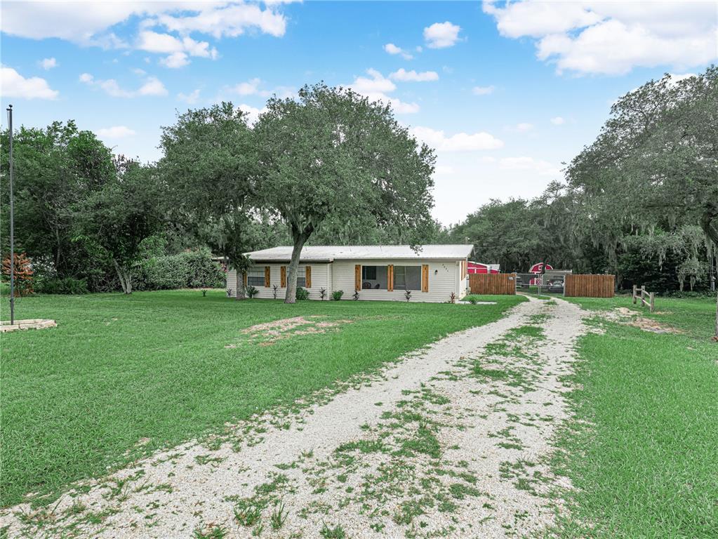 A single-story house with a gravel driveway sits on a grassy lot with large trees — 2935 N SILVER SPUR LOOP, LAKE WALES, FL