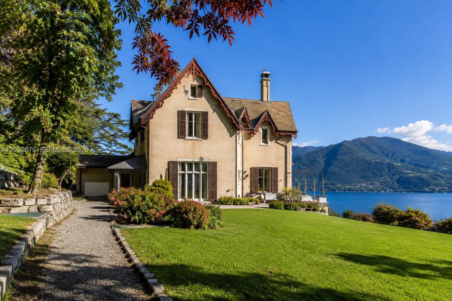 A two-story stucco house with decorative trim sits on a lawn overlooking a lake — Lake Como Luxury Real Estate for Sale Max Mlekus, FL