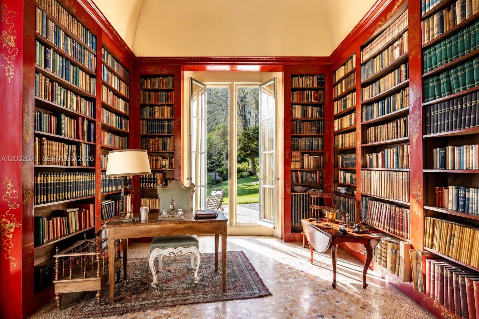 A home library with red lacquered bookshelves, a wooden desk, and French doors to a garden — Lake Como Luxury Real Estate for Sale Max Mlekus, FL