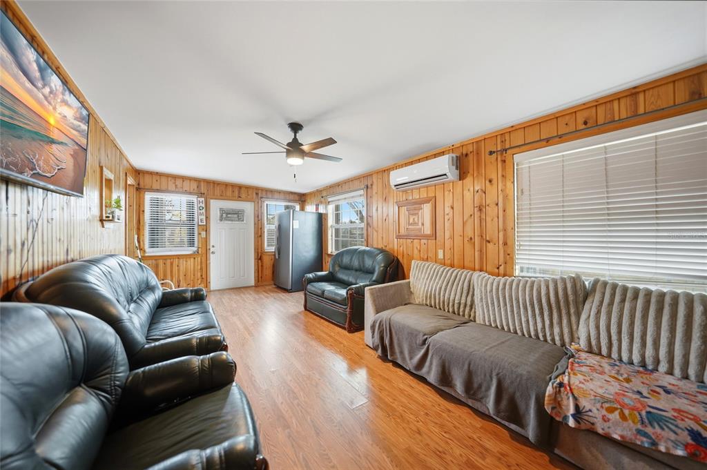 A living room with wood-paneled walls, hardwood floors, a ceiling fan, and multiple sofas — 658 VIA CALA, ENGLEWOOD, FL