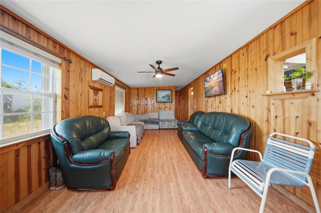 A living room features wood-paneled walls, wood-look flooring, two green leather sofas, and a ceiling fan — 658 VIA CALA, ENGLEWOOD, FL