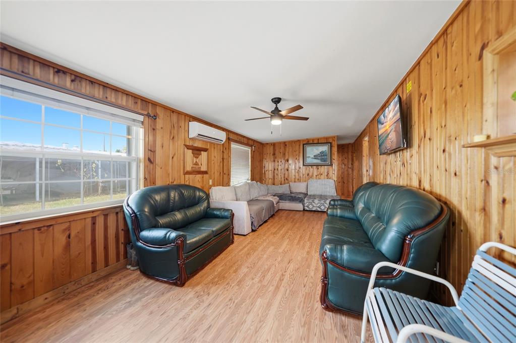 A living room features wood-paneled walls, light wood flooring, two green sofas, and a sectional — 658 VIA CALA, ENGLEWOOD, FL
