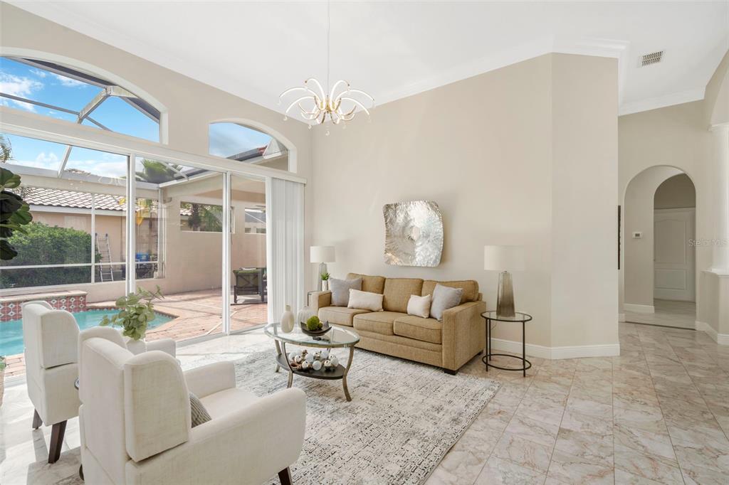 A living room features a beige sofa, two white armchairs, and sliding doors overlooking a pool — 5909 ZAKI LANE, APOLLO BEACH, FL