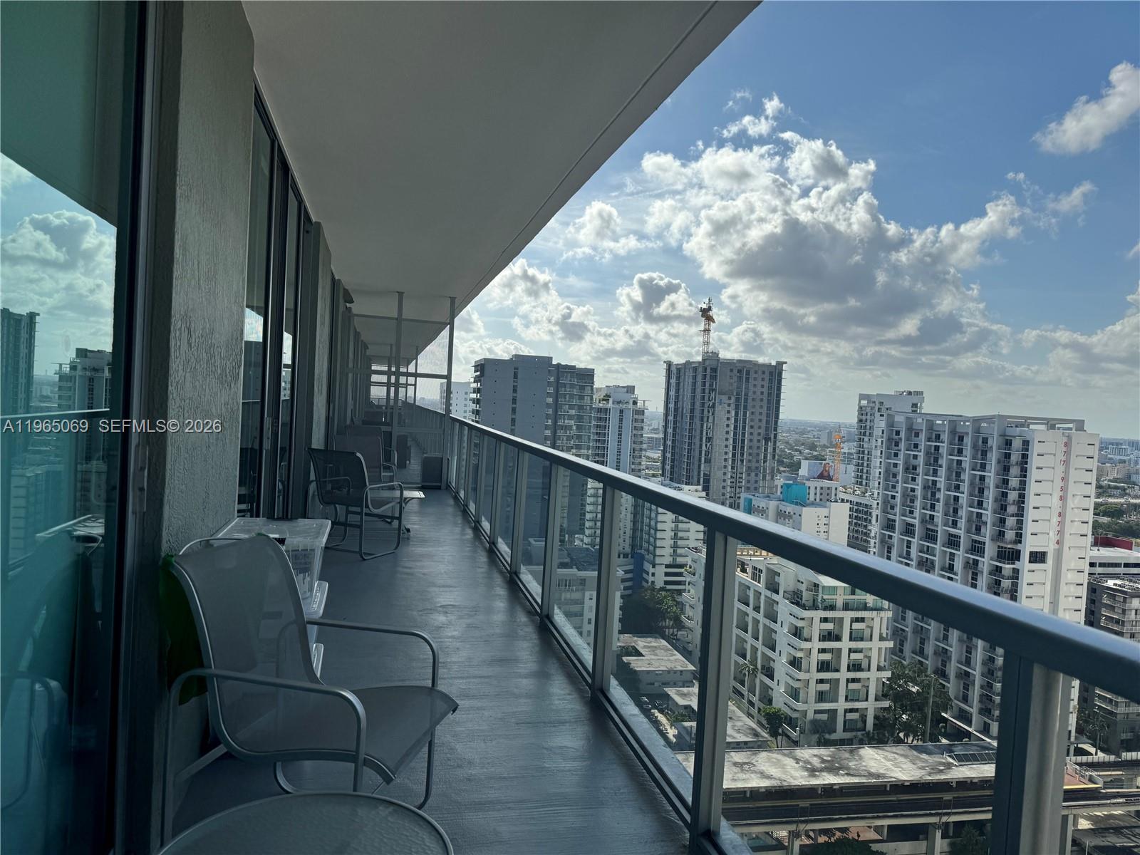 A high-rise balcony features metal chairs and a glass railing overlooking a city skyline — 1111 SW 1st Ave, Miami FL 33130, MIAMI, FL