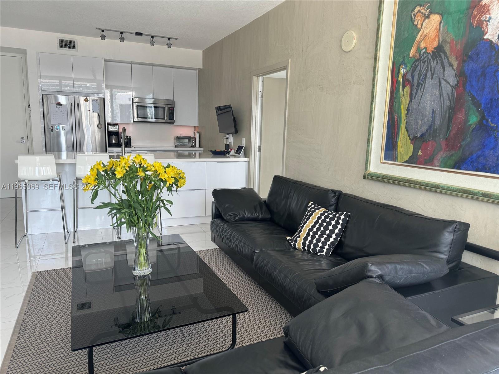 A living room with a black leather sofa, glass coffee table, and an open kitchen — 1111 SW 1st Ave, Miami FL 33130, MIAMI, FL